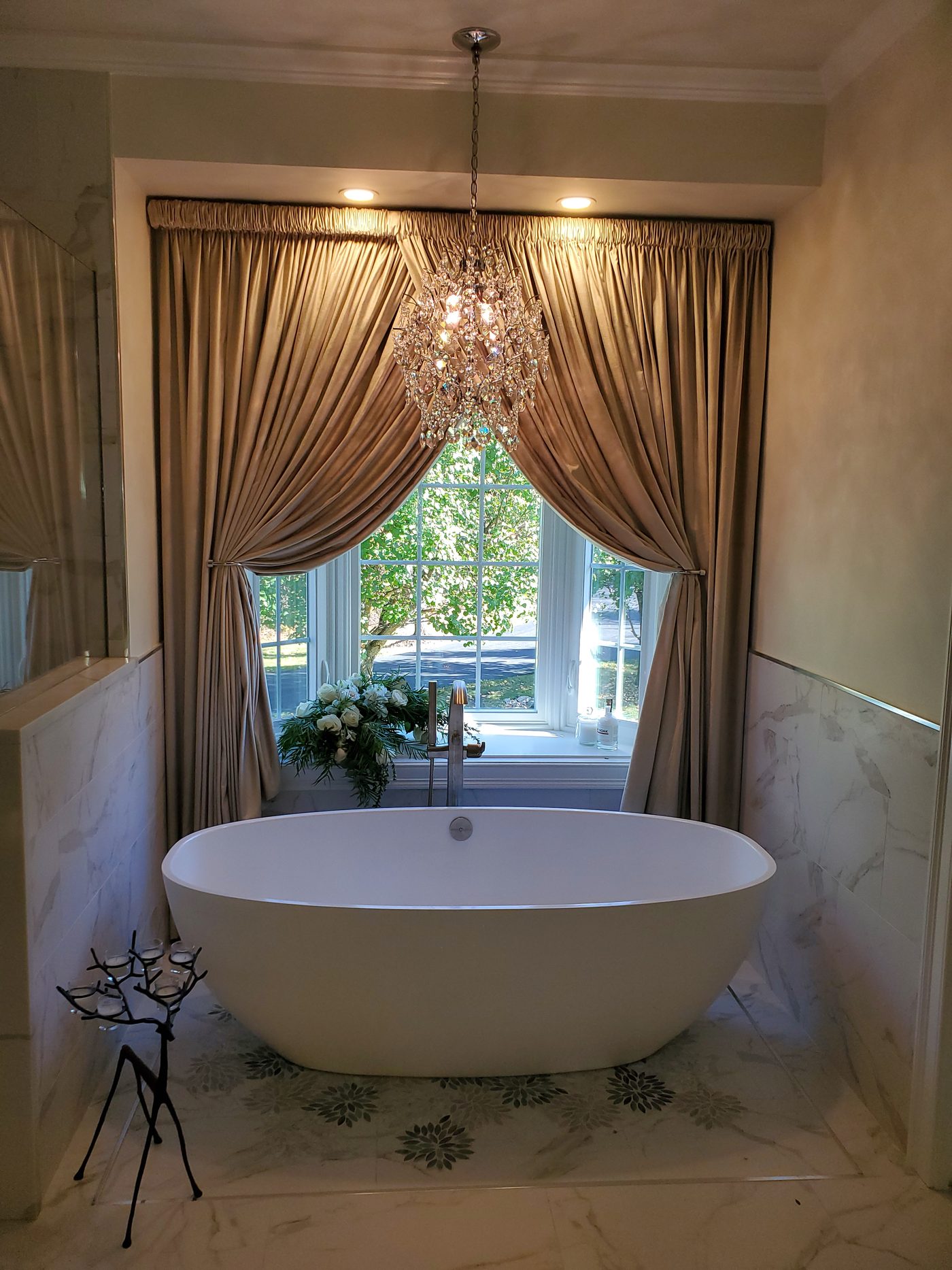 Freestanding soaking tub under a crystal chandelier with marble surround